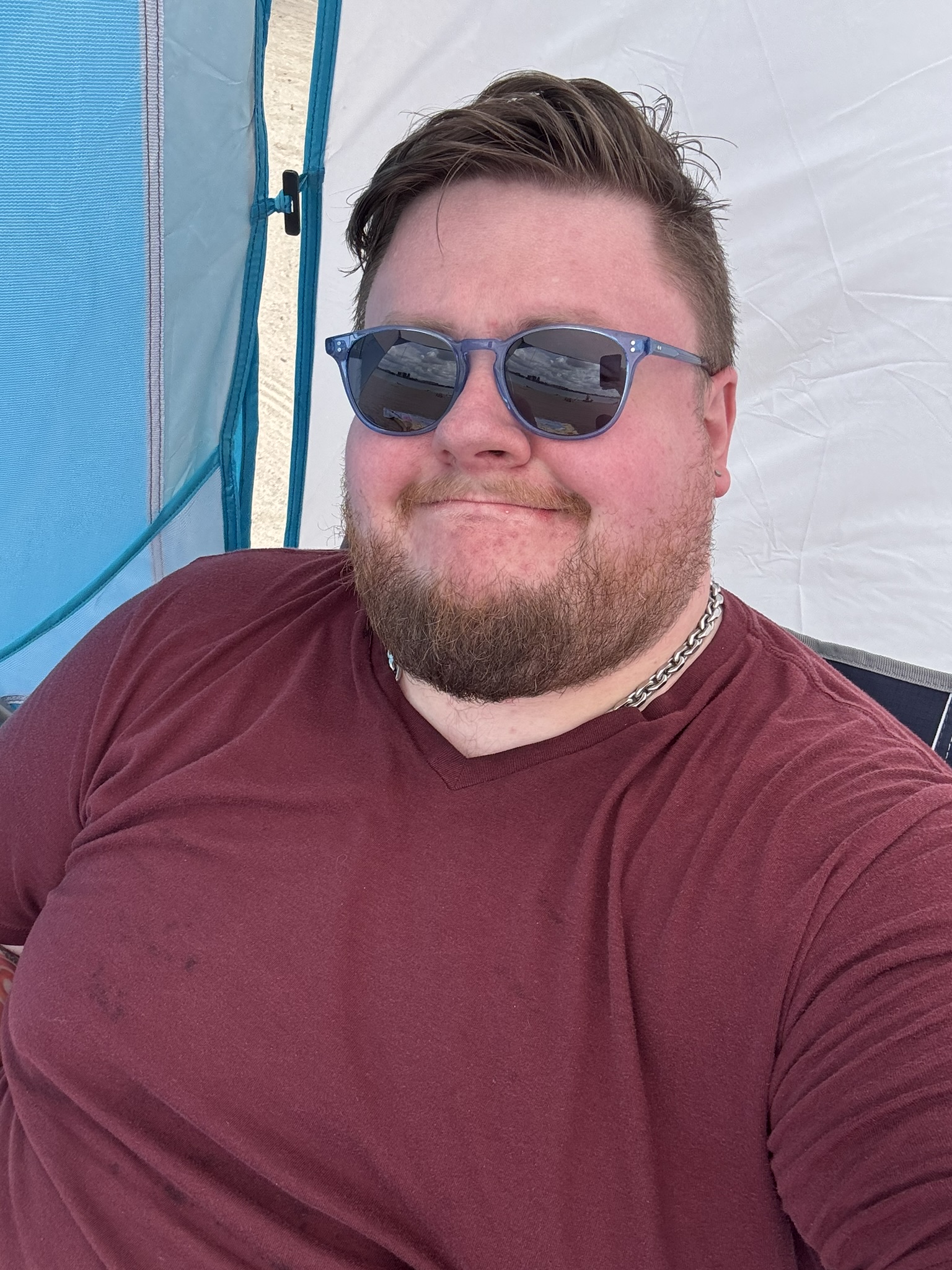 A man in a red shirt and sunglasses sitting against a blue and grey backdrop